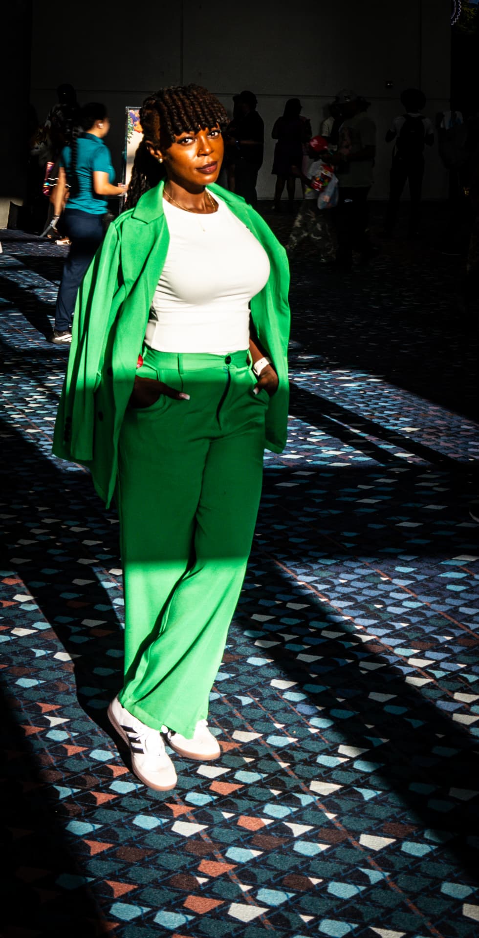 Woman in a bright green suit and white top standing in a beam of sunlight on a patterned convention carpet